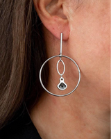 Elegant silver hoop earrings featuring a dangling Austrian crystal in Silver Night color, worn by a model.