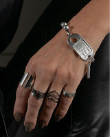 Chunky silver ball chain bracelet with an ID tag closure, worn on a hand adorned with multiple edgy rings.