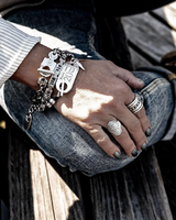 Chunky silver ball chain bracelet featuring a leather ID tag closure, worn stacked with stylish rings on a hand.