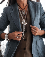 Person wearing a blue blazer with jewelry and a blurred outdoor background