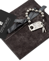 Chunky silver ball chain bracelet with a leather detail and an ID tag closure, presented on a soft gray velvet pouch.