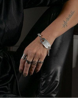 Chunky silver ball chain bracelet with leather and ID tag closure, styled on a model wearing a black blouse and leather pants.