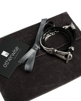 Black leather wrap bracelet featuring a funky silver clasp, presented on a dark suede pouch with a silver ribbon.