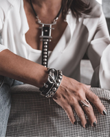 Black leather wrap bracelet featuring a funky silver clasp, layered with other stylish bracelets on a model's wrist.