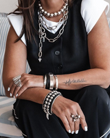 Person wearing multiple necklaces, bracelets, and rings sitting on a couch.