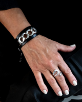 Hand wearing a black leather bracelet with chain detail on a dark background