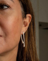Modern geometric droplet earrings in silver, featuring an irregular shape, worn comfortably on an earlobe.