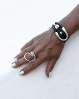 Hand wearing a black leather bracelet and silver rings on a white background