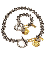 A silver-tone ball chain necklace with toggle clasp and gold-tone coin and tag charms, displayed on a clean white background.