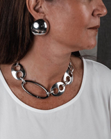 Chunky silver plated anchor link necklace worn on a model, paired with large metallic earrings and a white top.