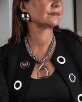 Person wearing a black jacket with circular cutouts and silver jewelry, including earrings and a necklace.