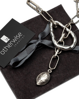 Silver necklace with a pendant on a dark surface with 'OtherWise Jewelry' card.
