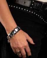 Hand wearing a silver bracelet with black nail polish against a dark background