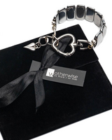 Silver bracelet with heart charm on a black box with 'otherwise' label