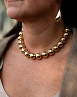 Close-up of a person wearing a gold necklace and earrings with a blurred background