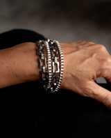 Multi-layer wrap bracelet with oxidized silver shark tooth pendant and heavy metal chains, worn on a wrist.