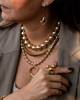 Close-up of a person wearing gold jewelry including necklaces, earrings, and rings.
