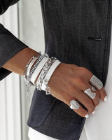 Person wearing multiple silver bracelets and rings on a plain background