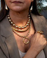 Woman wearing gold jewelry including a necklace and earrings outdoors.