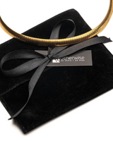 Gold necklace on a black velvet cushion with a black ribbon and 'Otherwise' brand tag.
