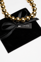 Gold necklace with black ribbon on a black pillow, branded 'otherwise'.