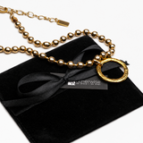 Gold necklace with a black bow on a black velvet pillow, branded 'Wutherwise'.