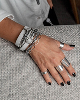 Hand wearing multiple silver bracelets and rings on a textured surface