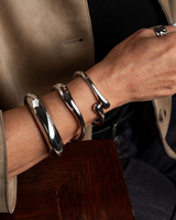 Three chunky metal cuff bangles in silver stacked on a model's wrist, showcasing a sleek, polished finish.