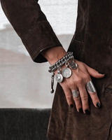 Chunky coin charm bracelet featuring a heavy metal curb chain with dangling antique-style coins and a leather closure.