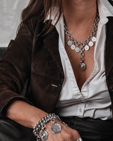 Chunky coin charm bracelet in silver with leather closure, featuring dangling antique-style coins, worn on wrist.