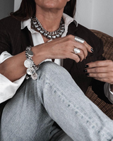 Chunky coin charm bracelet with leather closure displayed on a model's wrist, featuring metal coins and a sturdy leather strap.