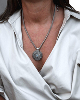 Layered leather and metal stacked necklace set worn on a model, featuring a braided silver chain and a large spiral pendant with a blue stone.