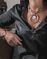 Chunky silver-plated chain necklace with bar closure and coin pendant, worn over a black satin shirt for an edgy look.