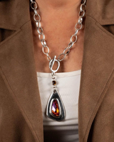 Chunky silver-plated necklace featuring a large red Austrian crystal pendant, worn over a white top with a brown blazer.