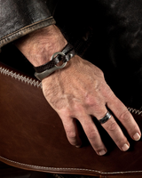 Unisex leather wrap bracelet in dark brown with a silver o-ring cuff, worn on a wrist resting on a leather surface.