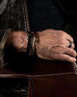 Unisex leather wrap bracelet featuring a silver-plated zamak o-ring cuff, worn on a wrist with casual leather attire.