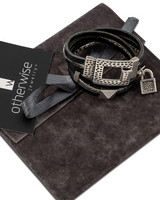Wrap around leather bracelet in black, featuring a hammered silver clasp and padlock charm, sits on a suede pouch.