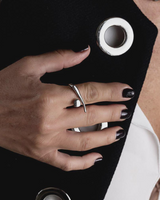 Asymmetrical stainless steel ring worn on the index finger, showcasing a smooth, curving design against a black jacket.