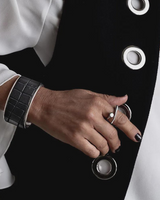 Adjustable stainless steel ring with a smooth, asymmetrical design worn on a model's finger, paired with a black leather cuff.