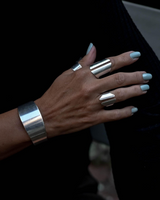 Chunky minimalist metallic cuffs, featuring an adjustable wide flat cuff and an open double band cuff, elegantly worn on a hand.
