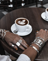 Chunky minimalist metallic cuffs stacked on a wrist, showcasing a mix of flat and open double band designs in silver.