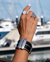 Wide black leather cuff bracelet with three silver-plated chains and two Zamak bars, worn on a model’s wrist.