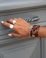 Triple wrap bracelet made of brown leather and sterling silver, worn stacked with chunky silver rings on a hand.