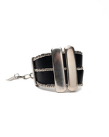 Wide black leather cuff bracelet featuring silver-plated Zamak bars and chain strands, showcasing an edgy rock style.