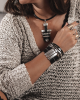 Wide black leather cuff bracelet with silver-plated bars, worn with layered metal bangles on a model in a cozy sweater.