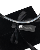 Black leather choker with curved gunmetal tube displayed on a soft black suede pouch with a ribbon tie.