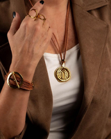 Natural leather strands in warm tones and a gold hammered metal hoop create a unique necklace worn over a white top.