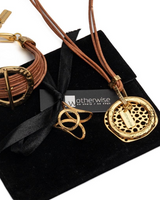 Natural leather strands form an edgy necklace featuring a gold-plated hammered metal hoop, presented on a black suede pouch.