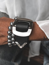 Wide black leather bracelet featuring a large silver buckle, worn as a statement piece with a chunky silver beaded bracelet.
