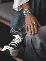 Chunky statement bracelet in antique silver plating with a bold design, worn on a wrist with denim and sneakers.